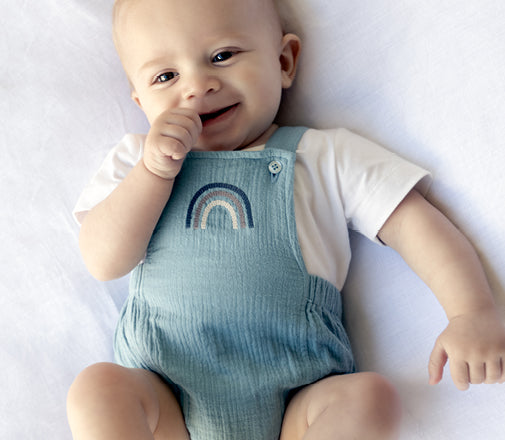 a baby boy smiling wearing a baby romper with a rainbow on the front